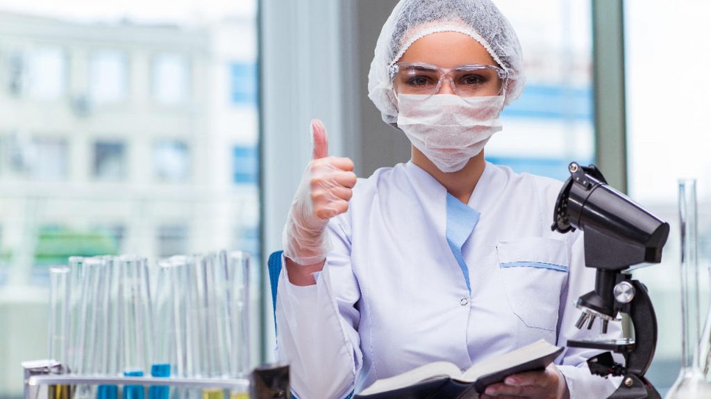 mulher com equipamento de laboratório segura um manual da qualidade fazendo positivo com o polegar