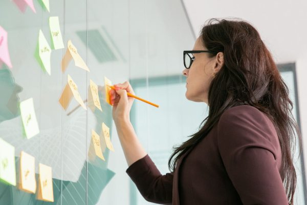 mulher escreve em postit colado em um quadro representando dinâmica de elaboração da visão missão e valores da empresa